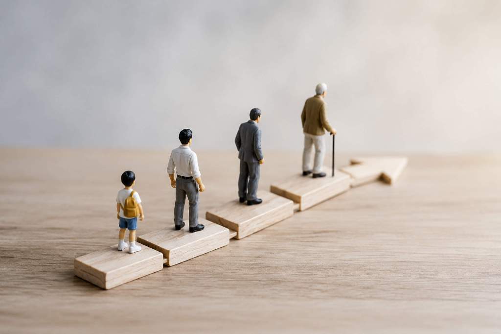 Miniature figures representing different life stages—from a child to an elderly adult—walking upward on staggered wooden blocks along a path shaped like an upward arrow